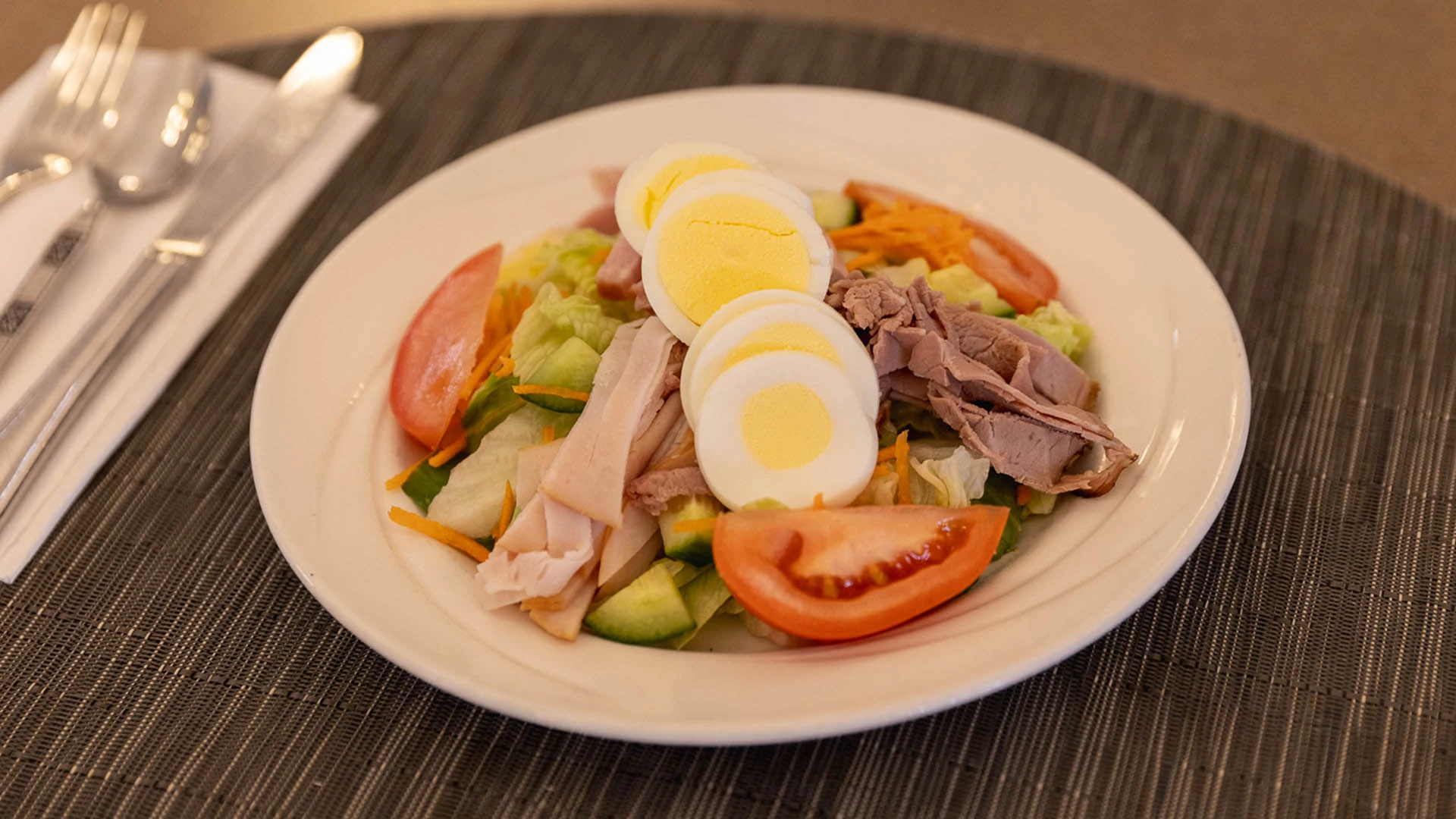 Green salad with hardboiled egg and sandwich meat on top